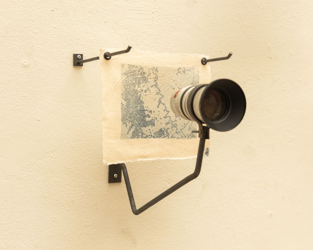 The patterns imprinted via cyanotype on textiles, and a surveillance camera lens look back at the audience.