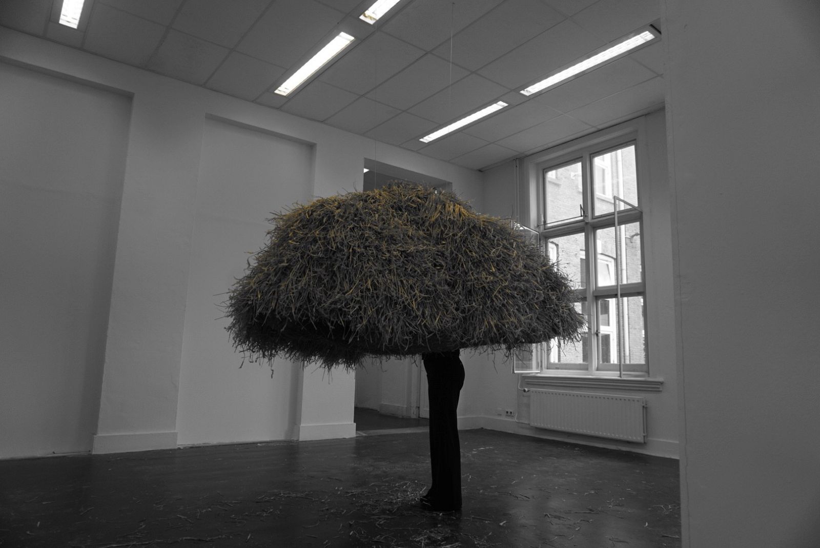 Person standing inside of straw sculpture shaped similarly to a nest. The person is visible from the feet to mid body.