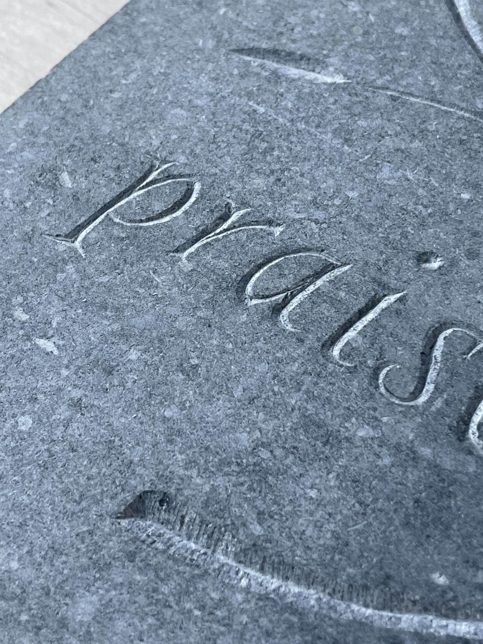 Closeup on a stone-carving, letters with a 3-dimensional, v-shaped cut, spelling 'praise'.