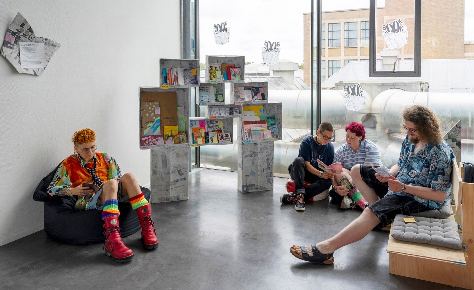 some people sitting on the floor on cushions and benches reading infront of the zine library